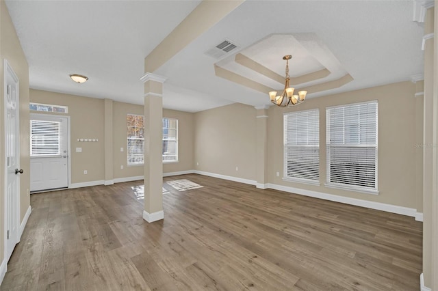 unfurnished living room with a tray ceiling, ornate columns, hardwood / wood-style floors, and an inviting chandelier