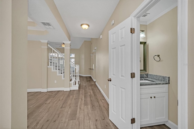 hallway with light hardwood / wood-style floors, crown molding, a textured ceiling, and vaulted ceiling