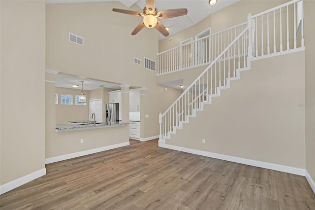 unfurnished living room with ceiling fan, sink, a towering ceiling, and wood-type flooring