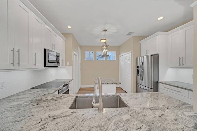 kitchen with white cabinetry, sink, hanging light fixtures, stainless steel appliances, and tasteful backsplash