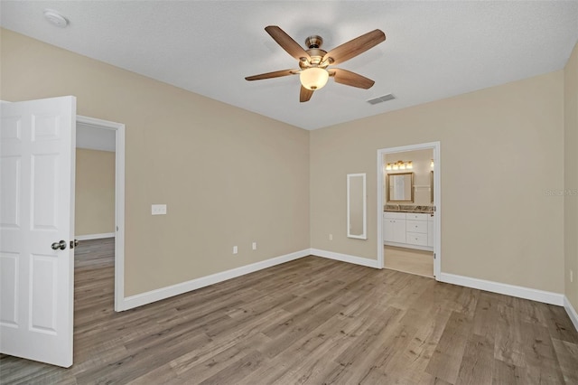 unfurnished bedroom featuring ceiling fan, light hardwood / wood-style floors, ensuite bathroom, and a textured ceiling