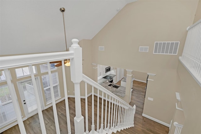 stairway with ceiling fan, hardwood / wood-style floors, and high vaulted ceiling