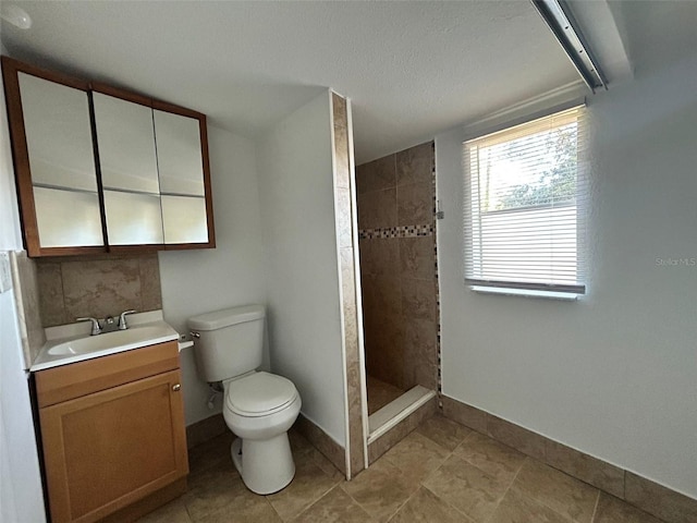 bathroom featuring a tile shower, vanity, a textured ceiling, and toilet