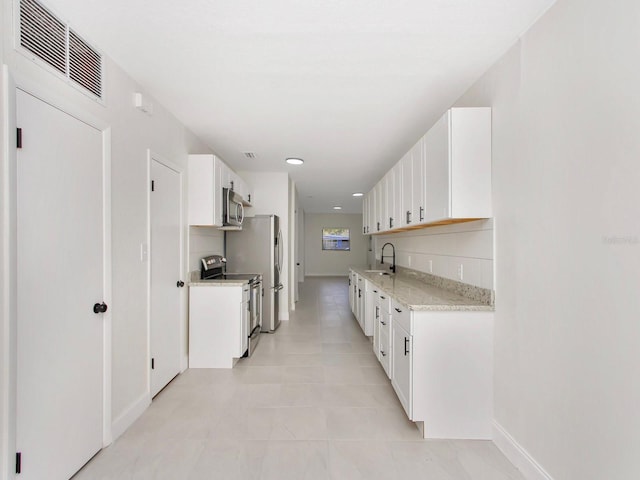 kitchen featuring sink, white cabinetry, light stone counters, light tile patterned floors, and appliances with stainless steel finishes