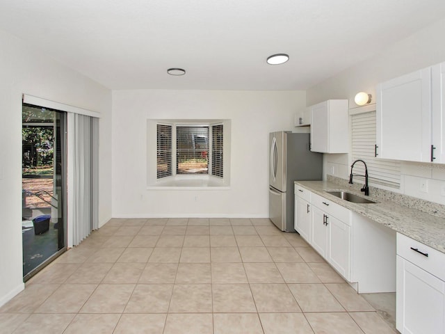 kitchen with light stone counters, white cabinetry, stainless steel refrigerator, light tile patterned flooring, and sink