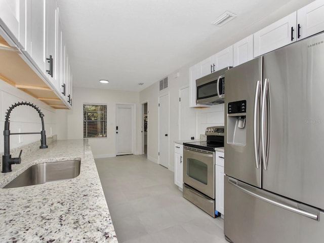 kitchen with appliances with stainless steel finishes, white cabinets, light stone counters, and sink