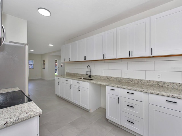 kitchen featuring sink, white cabinets, backsplash, and light stone counters