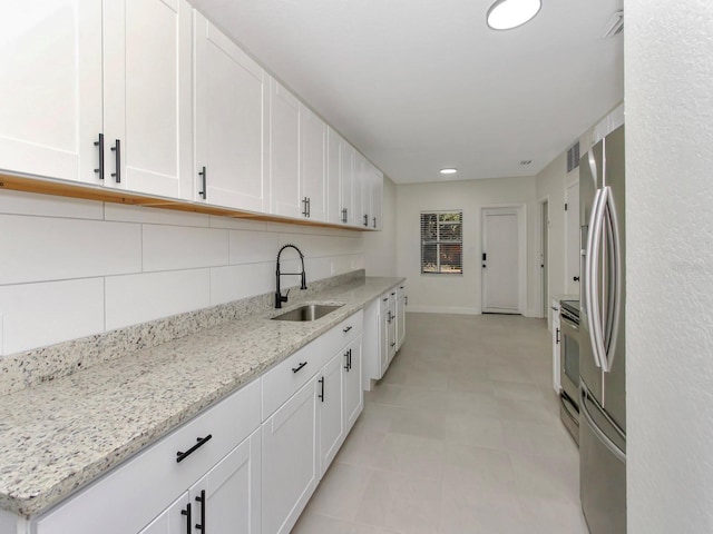 kitchen featuring light stone counters, white cabinets, tasteful backsplash, and sink