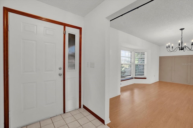 foyer entrance featuring light hardwood / wood-style flooring, a textured ceiling, and an inviting chandelier