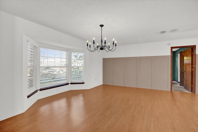 unfurnished dining area featuring a textured ceiling, light hardwood / wood-style flooring, and a chandelier