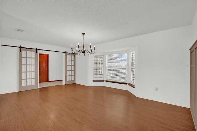 unfurnished room featuring wood-type flooring, a barn door, a textured ceiling, and a notable chandelier