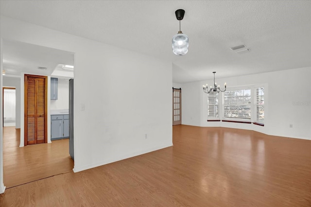 unfurnished living room featuring a chandelier, wood-type flooring, and a textured ceiling