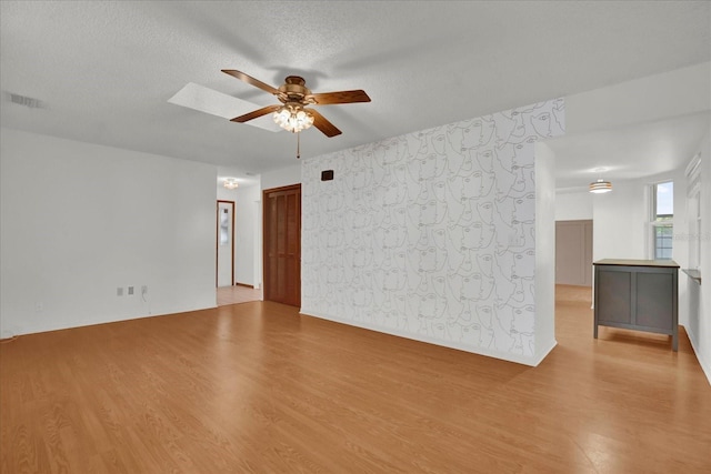 spare room featuring a skylight, a textured ceiling, light hardwood / wood-style floors, and ceiling fan