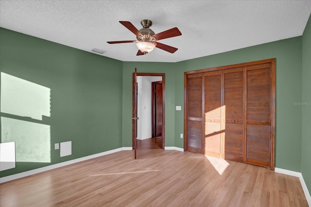 unfurnished bedroom with ceiling fan, light wood-type flooring, a textured ceiling, and a closet