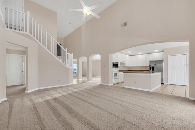 unfurnished living room with light colored carpet, high vaulted ceiling, and ceiling fan