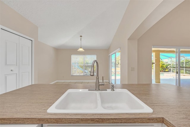 kitchen featuring a textured ceiling, sink, lofted ceiling, and hanging light fixtures