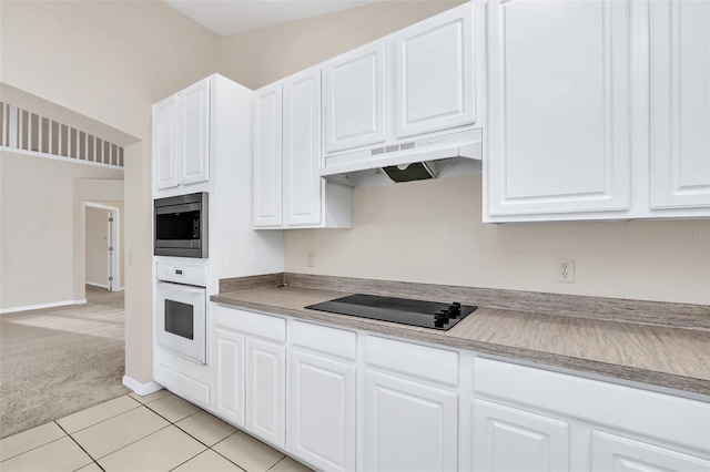 kitchen with stainless steel microwave, light carpet, oven, black electric cooktop, and white cabinetry