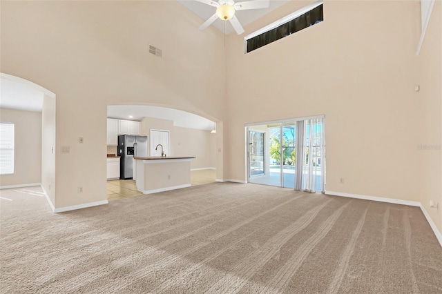 unfurnished living room with light carpet, sink, ceiling fan, and a high ceiling