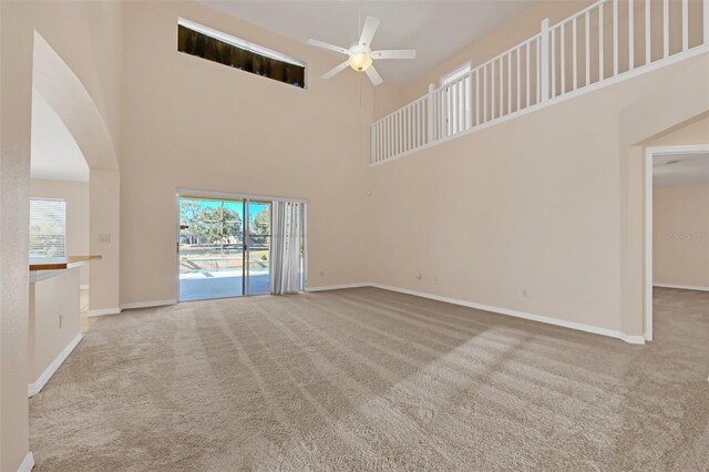 unfurnished living room featuring ceiling fan, light colored carpet, and a high ceiling