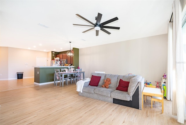 living room with ceiling fan with notable chandelier and light hardwood / wood-style flooring