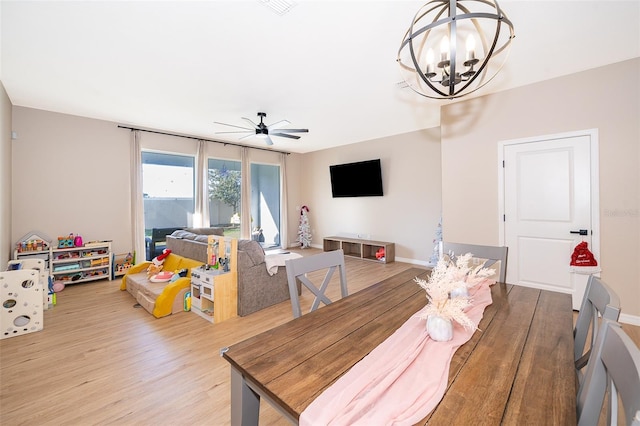 dining area with ceiling fan with notable chandelier and light hardwood / wood-style flooring