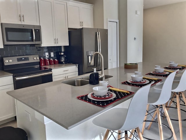 kitchen with a kitchen bar, stainless steel appliances, a kitchen island with sink, sink, and white cabinetry