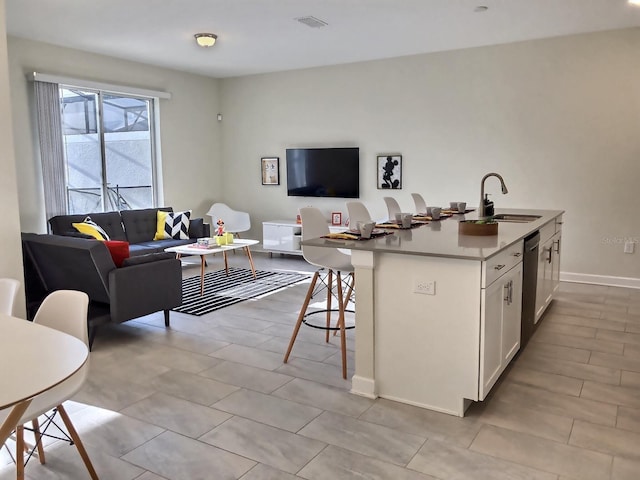 kitchen with a kitchen bar, sink, dishwasher, white cabinetry, and an island with sink