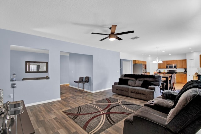 living room with a textured ceiling, ceiling fan with notable chandelier, and dark hardwood / wood-style floors