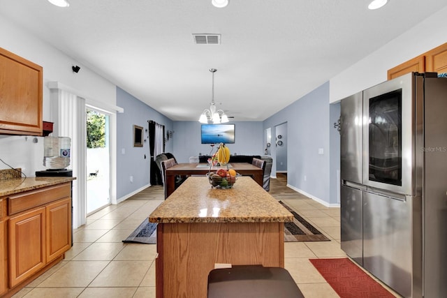 kitchen with stainless steel refrigerator, a center island, hanging light fixtures, light stone counters, and light tile patterned flooring