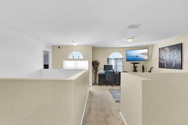 hallway featuring light colored carpet and a textured ceiling