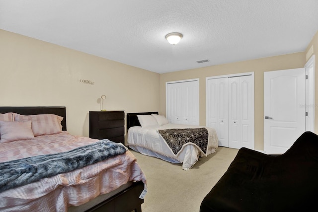 bedroom with two closets, a textured ceiling, and light colored carpet