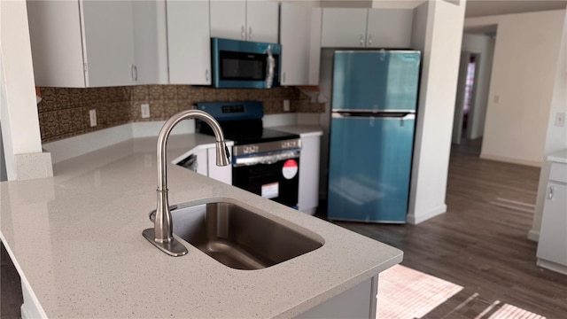 kitchen with light stone countertops, appliances with stainless steel finishes, dark wood-type flooring, sink, and white cabinets