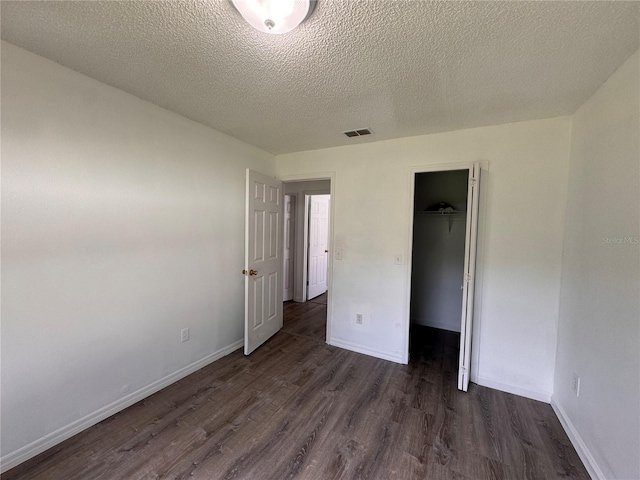 unfurnished bedroom featuring a textured ceiling, a walk in closet, dark wood-type flooring, and a closet