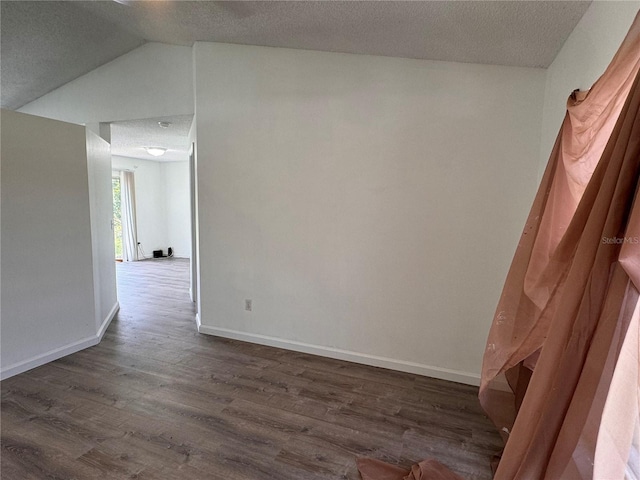 empty room featuring a textured ceiling, dark hardwood / wood-style flooring, and vaulted ceiling