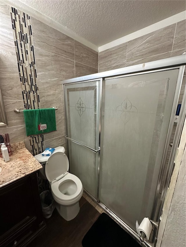 bathroom featuring vanity, toilet, a shower with shower door, and a textured ceiling