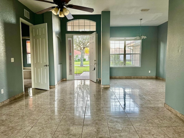 tiled spare room featuring ceiling fan with notable chandelier