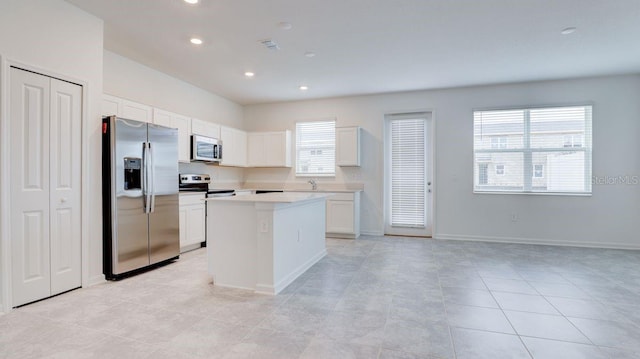 kitchen with a center island, sink, light tile patterned floors, white cabinetry, and stainless steel appliances