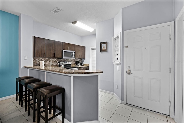 kitchen with kitchen peninsula, backsplash, dark brown cabinets, a textured ceiling, and stainless steel appliances