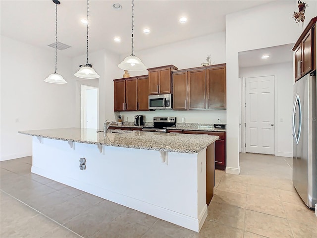 kitchen with light stone counters, an island with sink, decorative light fixtures, a breakfast bar area, and appliances with stainless steel finishes