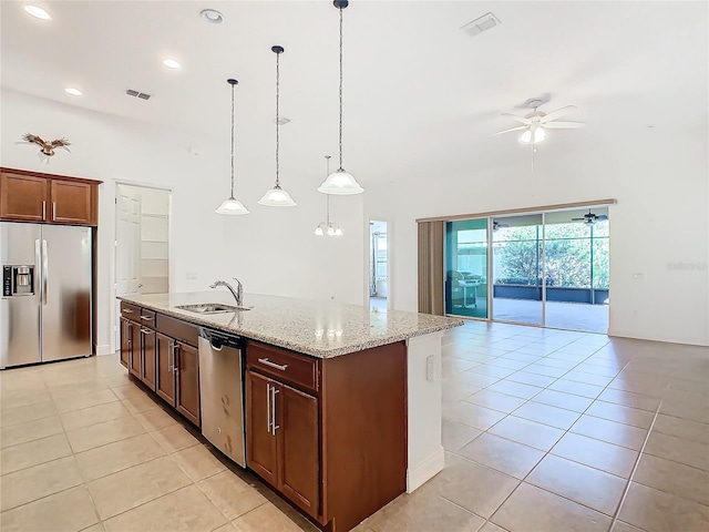 kitchen with light stone countertops, sink, stainless steel appliances, pendant lighting, and a kitchen island with sink