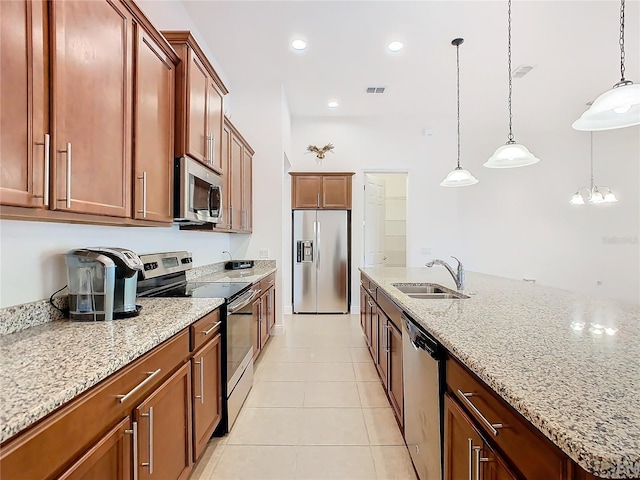 kitchen featuring a center island with sink, sink, light tile patterned floors, appliances with stainless steel finishes, and decorative light fixtures