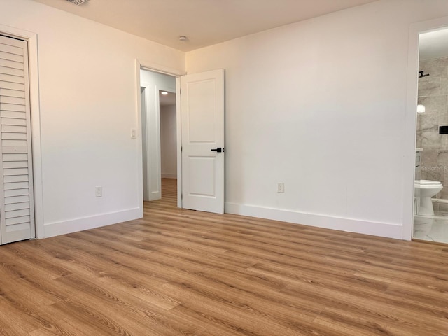 unfurnished bedroom with ensuite bathroom and light hardwood / wood-style flooring