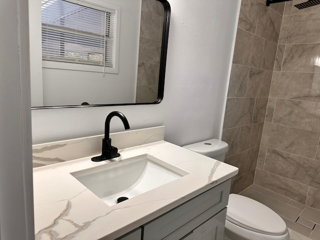 bathroom featuring a tile shower, vanity, and toilet