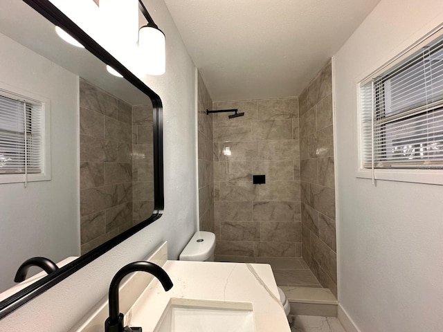 bathroom with toilet, a tile shower, and vanity