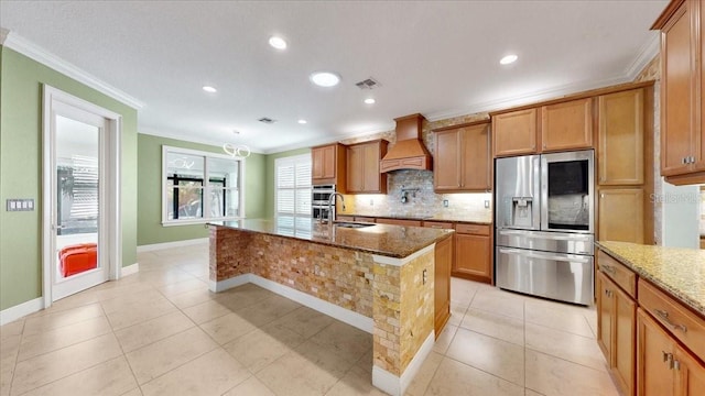 kitchen with light stone counters, custom exhaust hood, stainless steel appliances, a kitchen island with sink, and sink