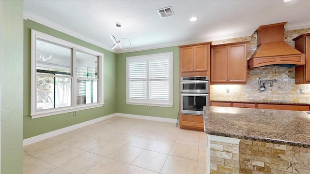 kitchen with double oven, a wealth of natural light, dark stone counters, and ornamental molding