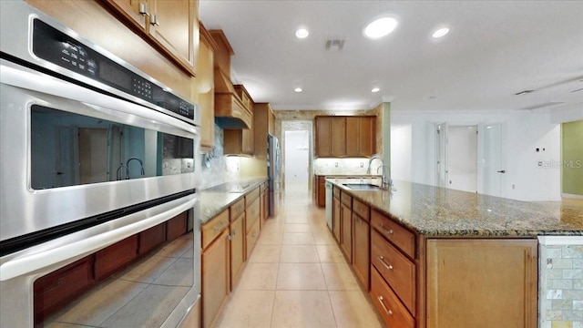 kitchen with light stone countertops, stainless steel appliances, sink, light tile patterned floors, and an island with sink