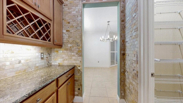 kitchen with an inviting chandelier, backsplash, pendant lighting, stone countertops, and light tile patterned floors