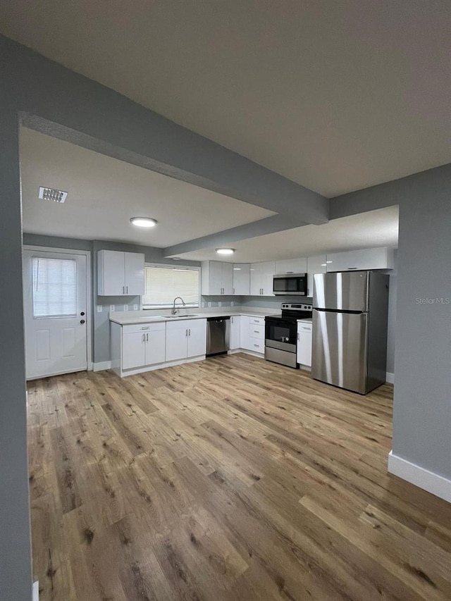 kitchen with sink, white cabinetry, stainless steel appliances, and light hardwood / wood-style flooring