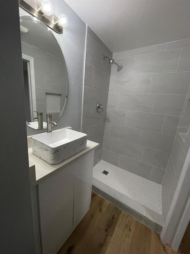 bathroom with hardwood / wood-style flooring, vanity, and tiled shower